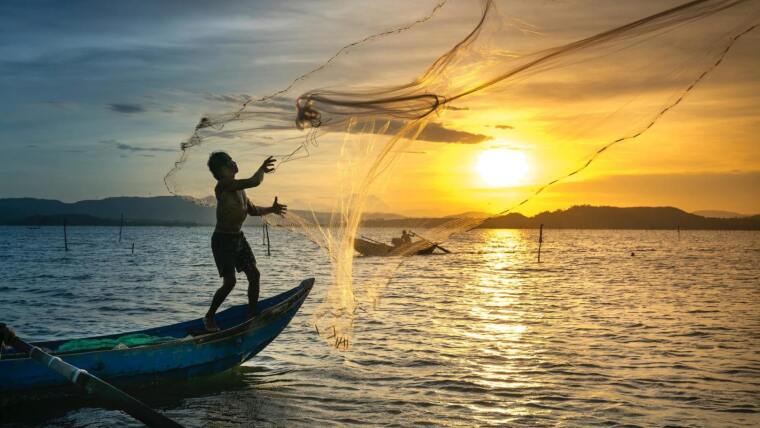 Ein Fischer wirft ein Netz im Sonnenaufgang auf.